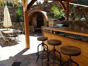 An outdoor patio with a stone wall, a wooden pergola, a brick oven, and a bar area with stools. - A FEW STEPS FROM THE SEA, MAS DES PORTALS CRIQUES MAGNIFICENT VIEW, (COLLIOURE)