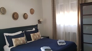 A hotel room with a bed, a nightstand, a lamp, a wall-mounted hat display, and a window with curtains. - A FEW STEPS FROM THE SEA, MAS DES PORTALS CRIQUES MAGNIFICENT VIEW, (COLLIOURE)