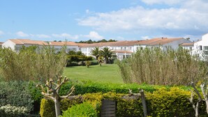 Fileira de edifícios brancos com telhados de telha vermelha, um jardim bem cuidado e diversos arbustos e árvores em primeiro plano.