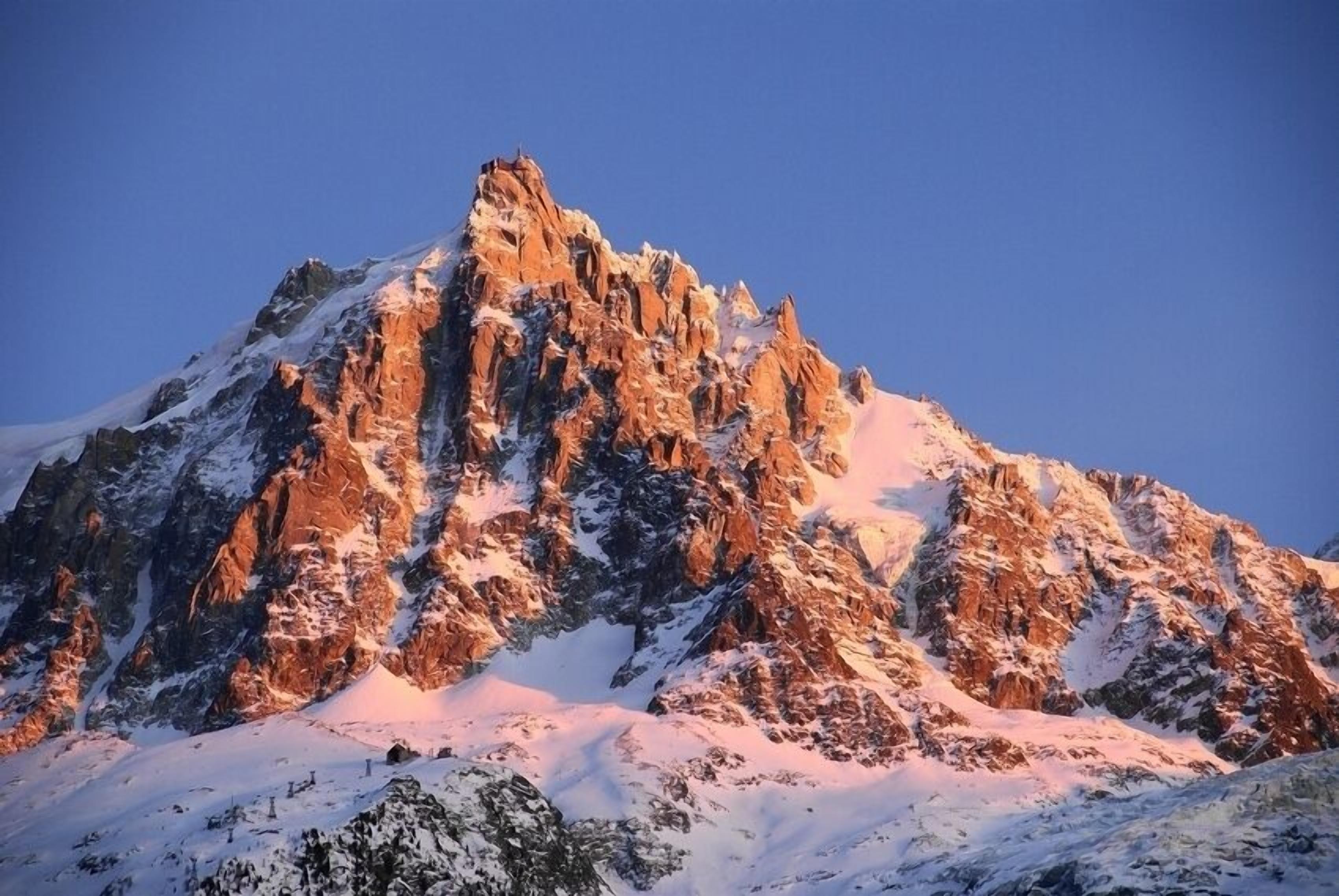 A snow-covered mountain peak with rugged terrain and a clear sky.