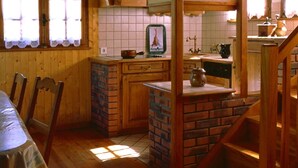 Puinen sisustus, jossa on keittiöalue, ruokapöytä tuoleineen ja portaikko.