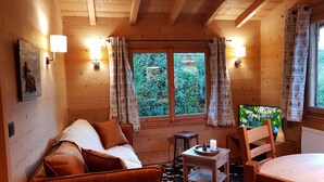 A cozy cabin interior with wooden walls, a sofa, a small table with a candle, and a window with curtains.