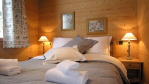 A cozy wooden cabin room with a bed, two bedside lamps, and two framed pictures on the wall.