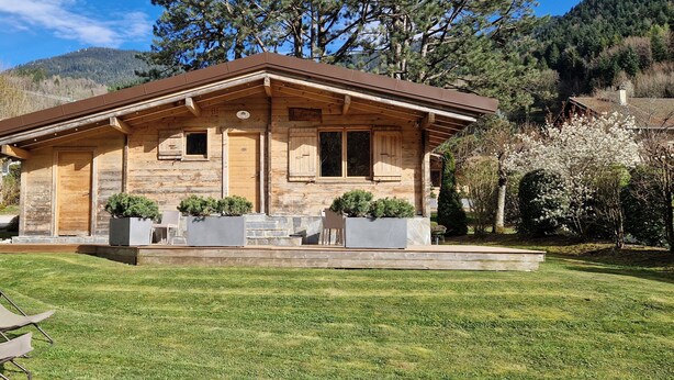 A wooden cabin with a sloped roof, stone foundation, and a small porch with seating.