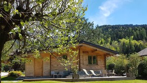 A wooden cabin with a covered patio, outdoor seating, and a view of a forested hillside.
