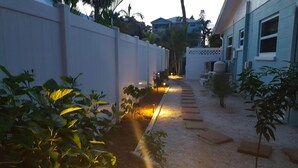 A pathway flanked by white walls and plants, leading to a building with a blue exterior.
