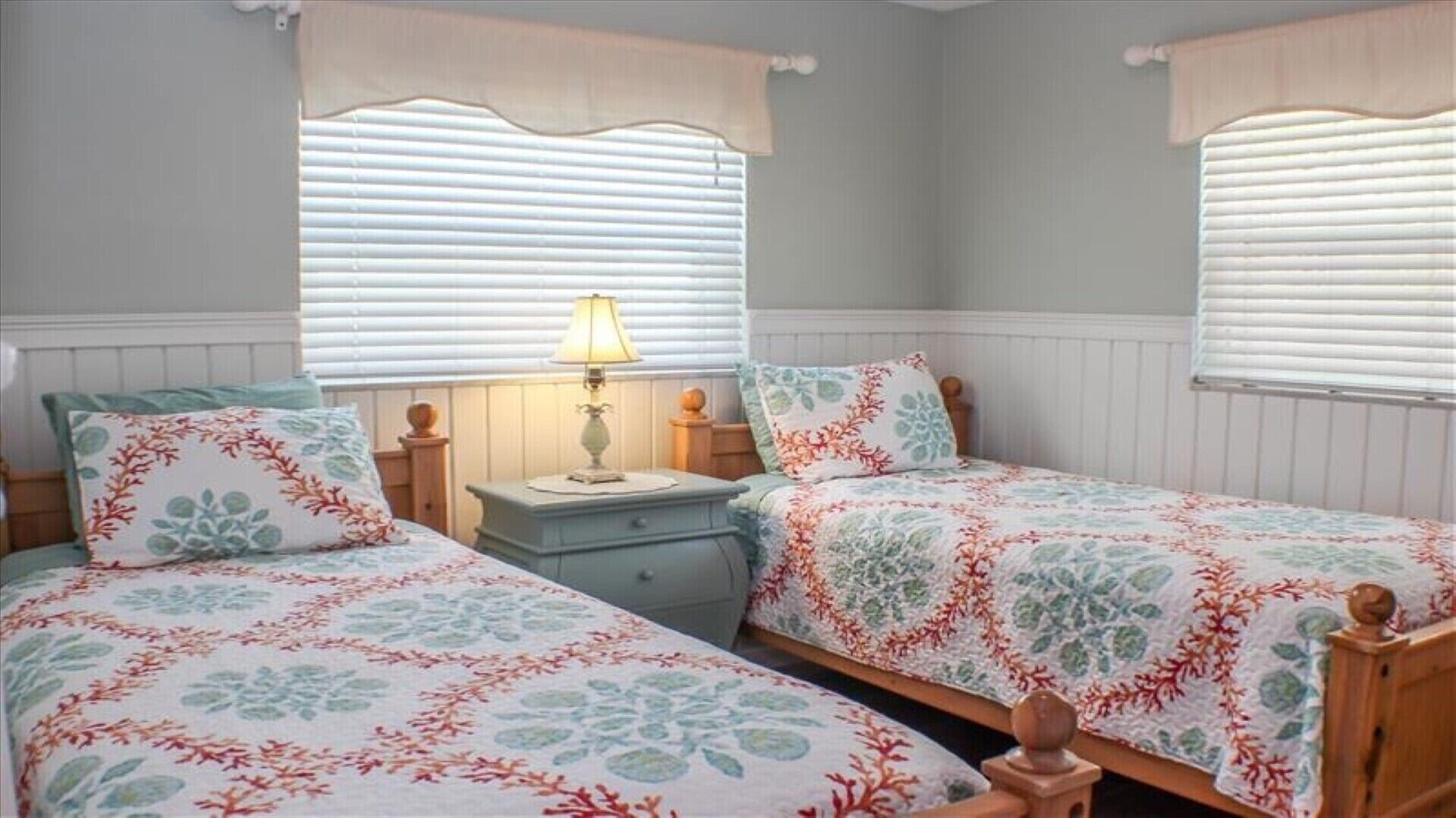 Un dormitorio con dos camas individuales, una mesita de noche con lámpara y una ventana con persianas.