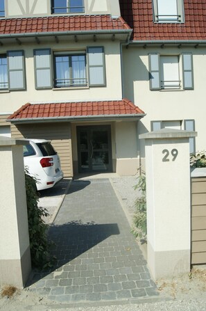 A residential building with a red-tiled roof, a gated entrance, and a white car parked in the driveway.