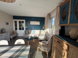 A living room with a sofa, a coffee table, a wooden cabinet, and a dining area with chairs and a table.