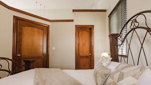 Une chambre à coucher avec un lit, des portes en bois, une tête de lit en métal et une fenêtre avec des stores.