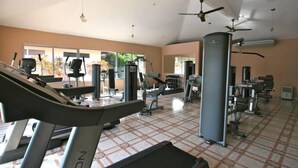 Une salle de sport équipée de tapis de course, d’appareils de musculation et de ventilateurs au plafond.