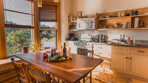 A kitchen with wooden cabinets, a dining table, and a window with blinds. - Contemporary Apartment in Historic 1895 Building (Hardwick)