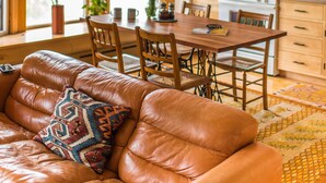 A cozy living room with a leather sofa, a dining table, and chairs. There is a kitchen area with a microwave, stove, and cabinets. - Contemporary Apartment in Historic 1895 Building (Hardwick)