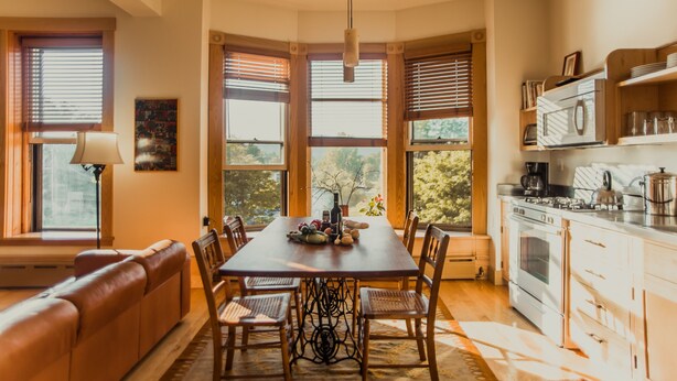 A dining area with a wooden table, chairs, and a view through large windows. - Contemporary Apartment in Historic 1895 Building (Hardwick)