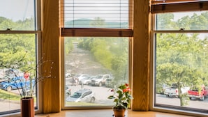 A view through a window with wooden blinds, a stop sign, and a parking lot with cars and greenery. - Contemporary Apartment in Historic 1895 Building (Hardwick)