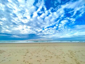 Une plage où l’on voit des empreintes dans le sable et un ciel nuageux.