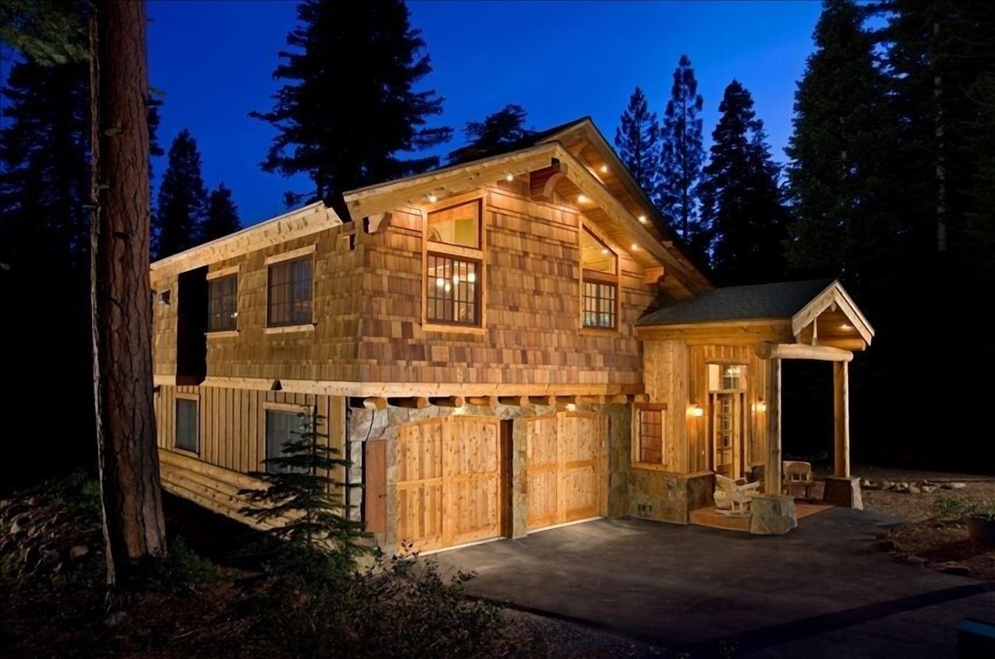 A wooden cabin with a large garage, a covered porch, and a small attached structure.
