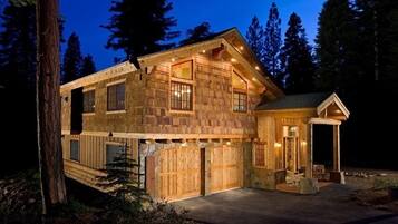 A wooden cabin with a large garage, a covered porch, and a small attached structure.