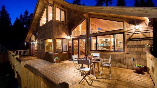 Une cabane en bois dotée d’une terrasse, de grandes fenêtres et d’un escalier menant à l’étage supérieur.