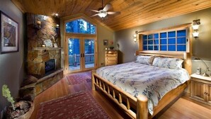 Une chambre avec une cheminée en pierre, un plafond en bois, un grand lit et une vue sur l’extérieur grâce à une porte vitrée.