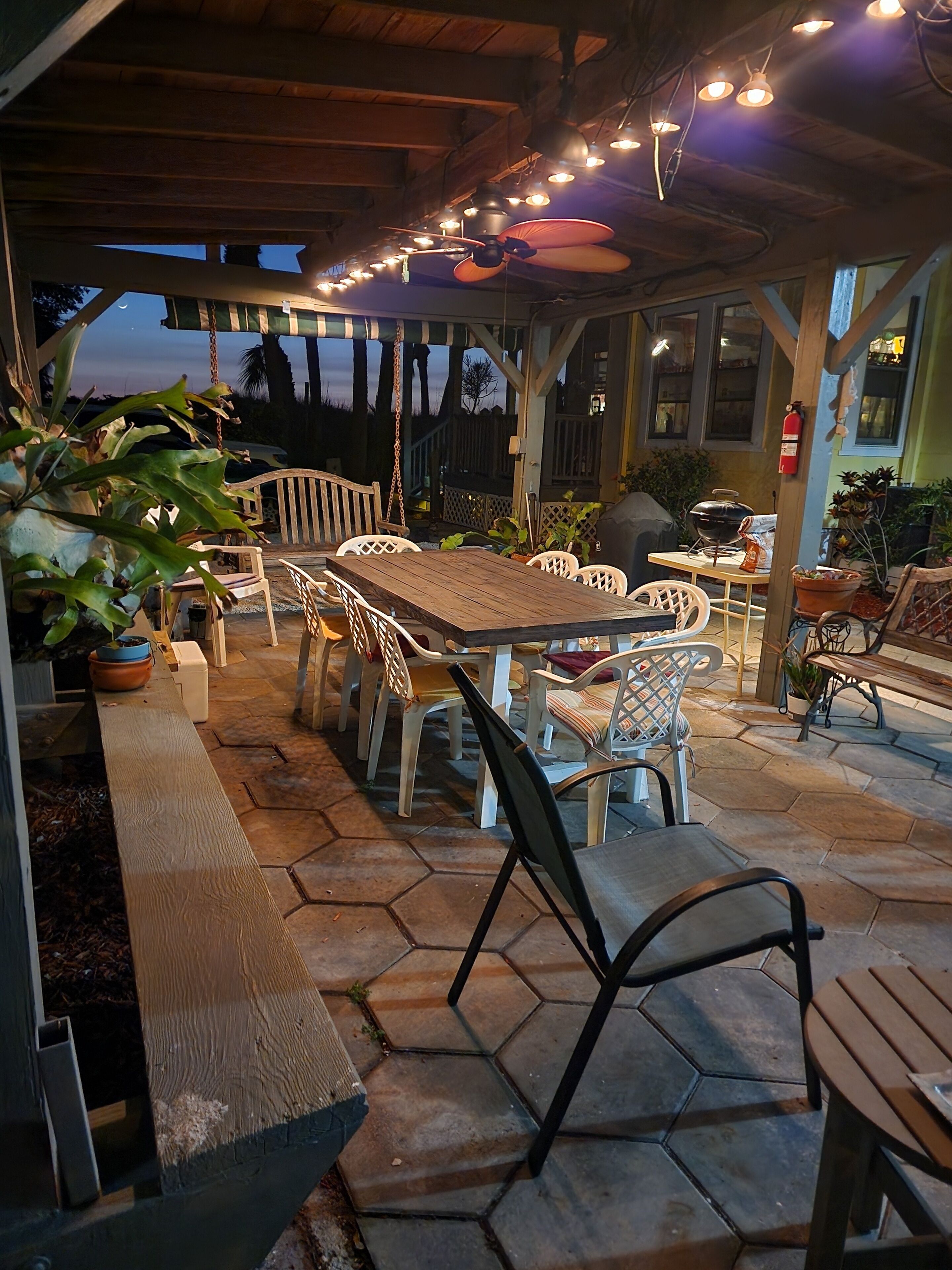 Un espace extérieur aménagé en terrasse, avec une table et des chaises en bois, entouré de plantes en pot et doté d’un sol en pierre.