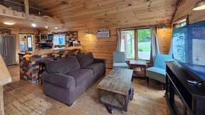 A cozy cabin interior with a wooden ceiling, a kitchenette, a sofa, a coffee table, and a TV. - Sight distance of Lake Superior Beach, Autrain River, Close to Pictured Rocks (Au Train)
