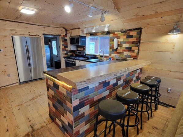 Une cuisine moderne dotée d’un îlot central en bois, de tabourets de bar, d’appareils électroménagers en acier inoxydable et d’un revêtement mural coloré.