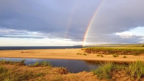A beach with a visible rainbow, a calm body of water, and grassy dunes. - Sight distance of Lake Superior Beach, Autrain River, Close to Pictured Rocks (Au Train)