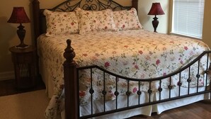 A bedroom with a wooden bed frame, floral bedding, two bedside lamps, and a window with blinds.