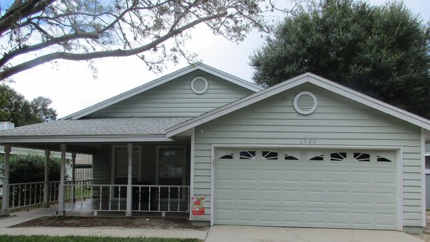 Une maison de plain-pied avec un garage, une véranda et un petit jardin devant.