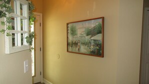A hallway with a painting of a street scene, a door, and a window with ivy.