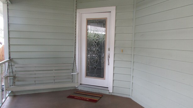 A white door with a glass panel and a metal handle, a small step leading to the door, and a welcome mat on the porch.