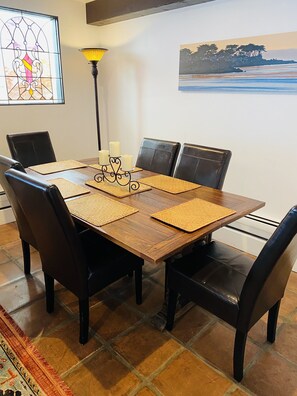 A dining area with a wooden table, black leather chairs, woven placemats, and candles.