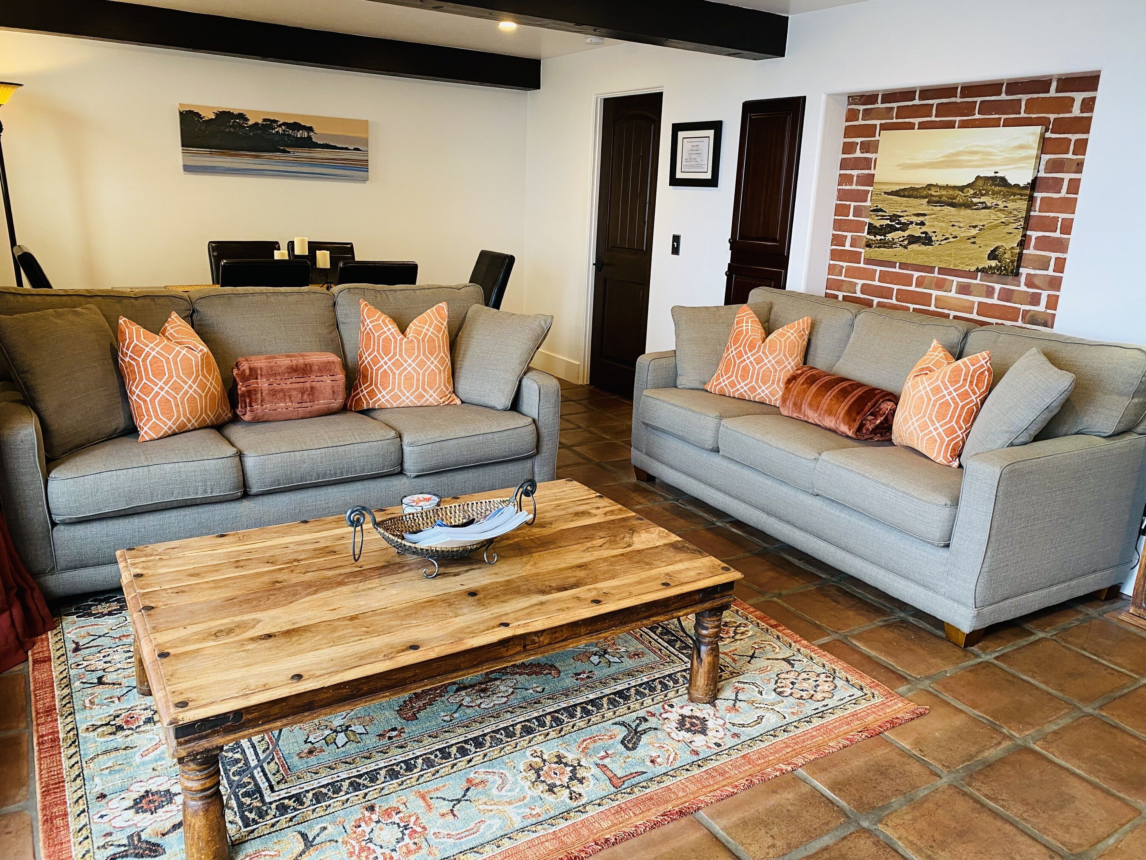 Un salon avec deux canapés gris, des coussins à motifs, une table basse en bois et un tapis décoratif.