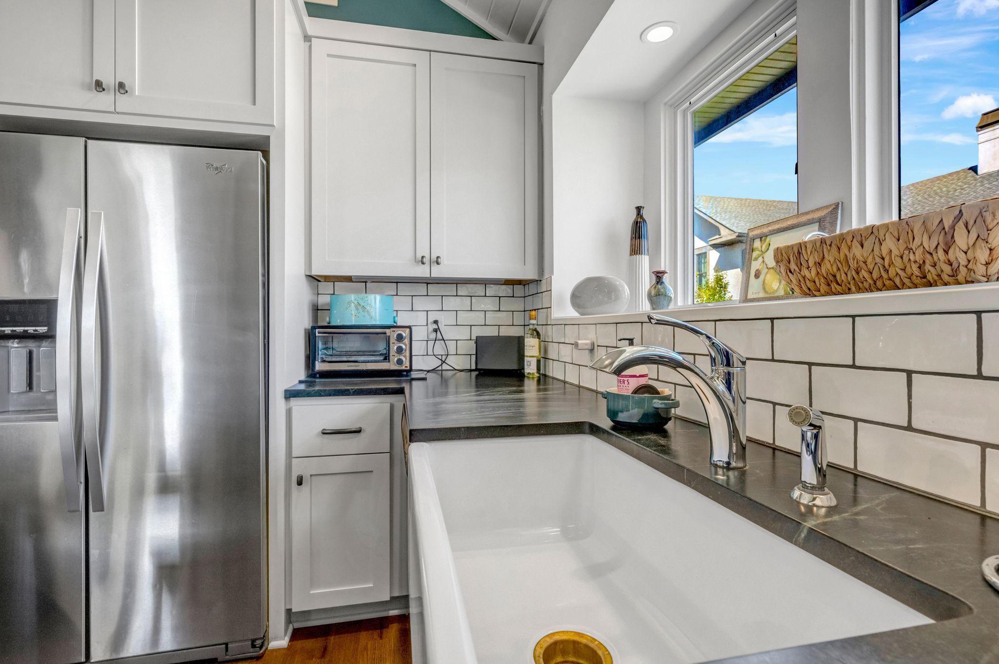 A modern kitchen with white cabinets, stainless steel appliances, a black countertop, and a window providing natural light.
