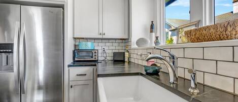 A modern kitchen with white cabinets, stainless steel appliances, a black countertop, and a window providing natural light.