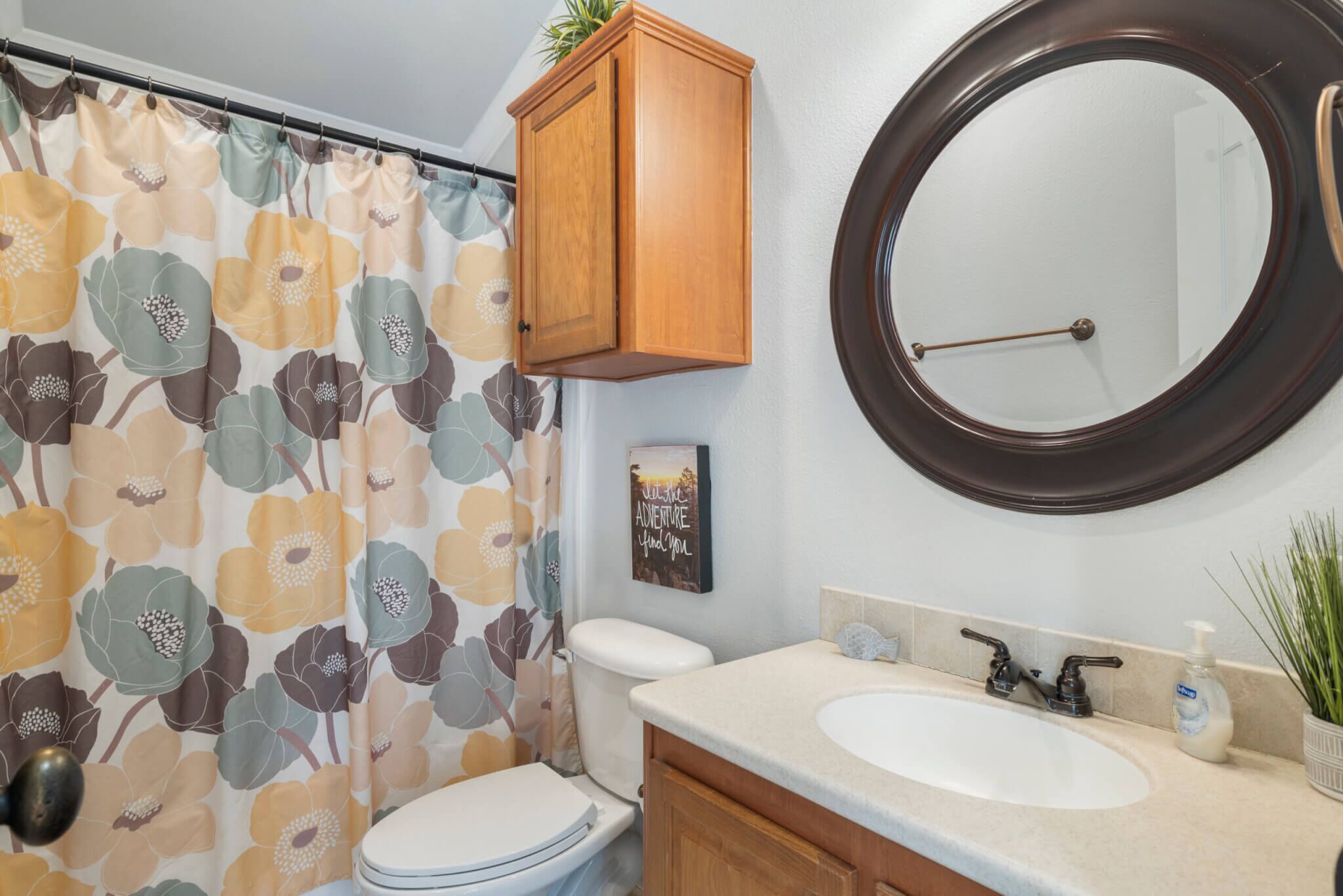 Un baño con inodoro, lavamanos con espejo y cortina de ducha estampada con motivos florales.