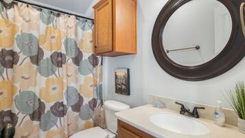 Un baño con inodoro, lavamanos con espejo y cortina de ducha estampada con motivos florales.