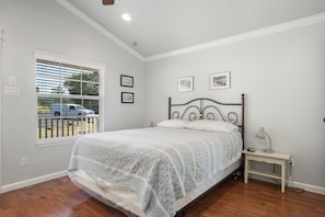 Un dormitorio con cama, mesita de noche, ventana con persianas e imágenes enmarcadas en la pared.