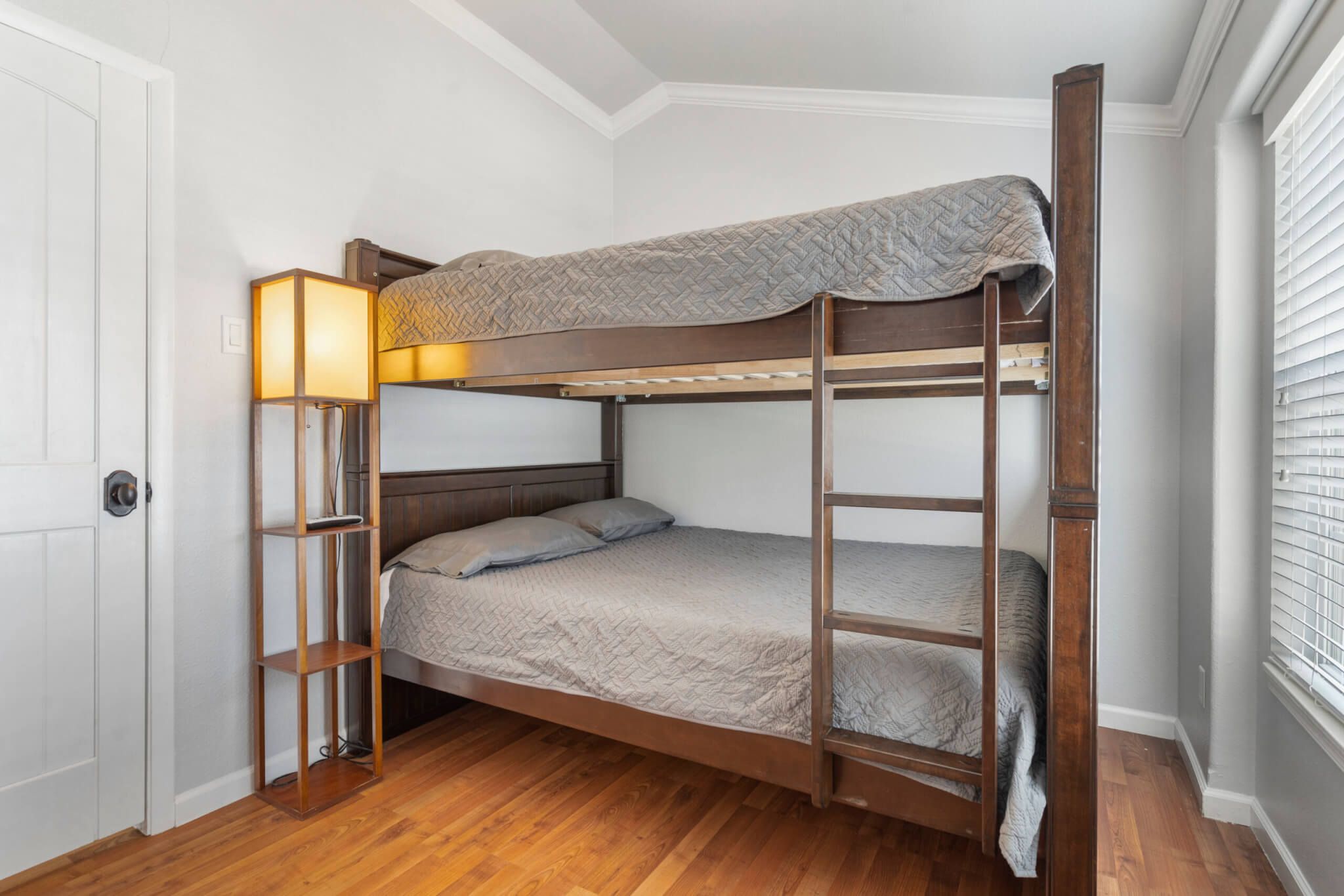 A bunk bed with a ladder, a bedside table with a lamp, and a door.