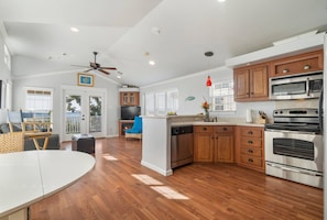 A modern kitchen with wooden cabinets, stainless steel appliances, and a dining area with a white table and chairs. - Rockport at CrossTimbers Marina (Sperry)