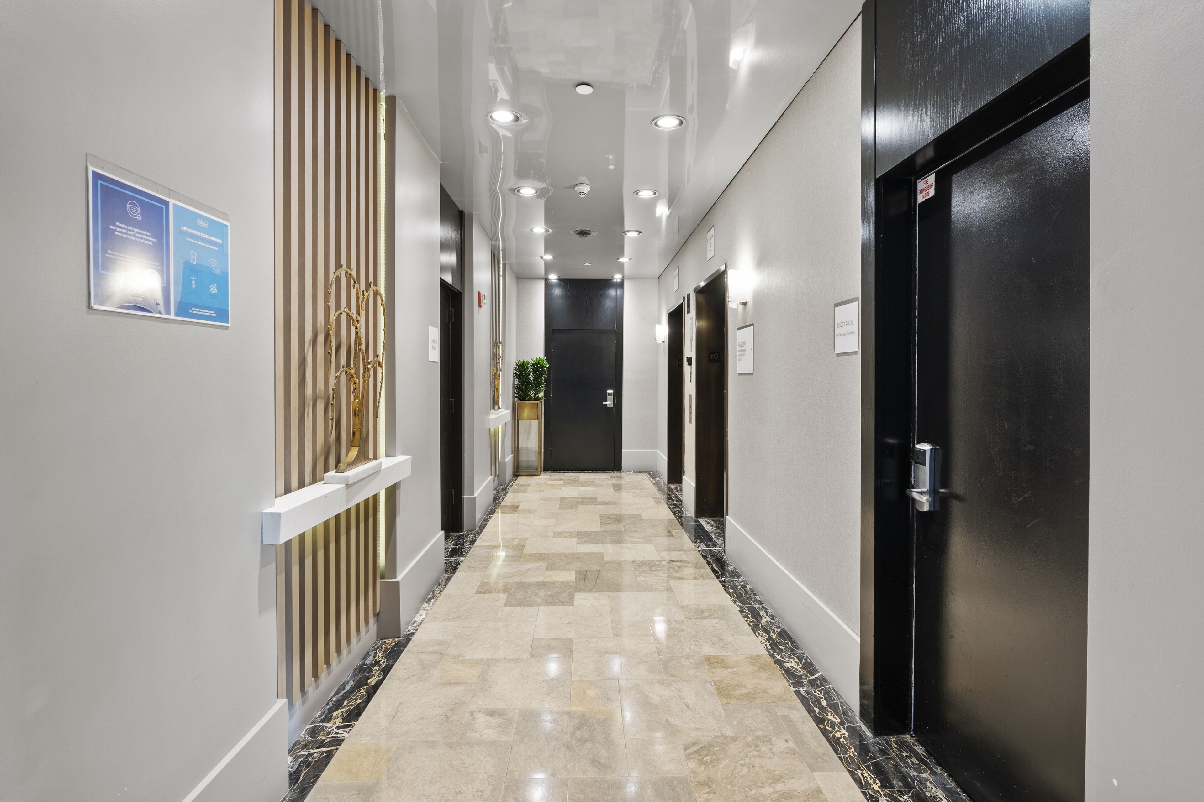 Un pasillo moderno con piso de mármol, puertas negras e iluminación empotrada.