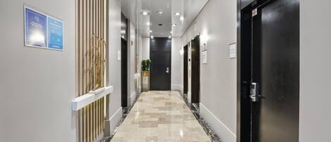 Un pasillo moderno con piso de mármol, puertas negras e iluminación empotrada.