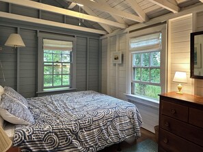 A bedroom with a bed, two windows, a dresser, and a lamp.