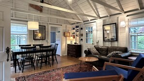 A spacious living room with a high ceiling, wooden beams, a dining area with a table and chairs, a leather sofa, and a patterned rug. - Peaceful hideaway on Westport Point (Westport)