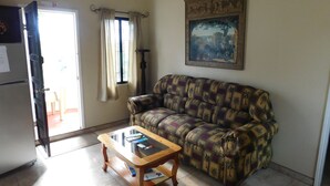 A living room with a sofa, a coffee table, a painting on the wall, and a door leading to a balcony.