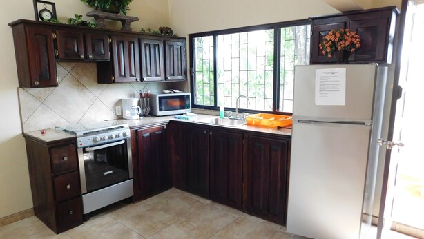 A kitchen with dark wooden cabinets, a white refrigerator, a microwave, a stove, and a sink.