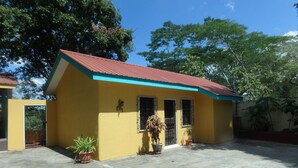 A yellow building with a red roof, a gated entrance, and potted plants.