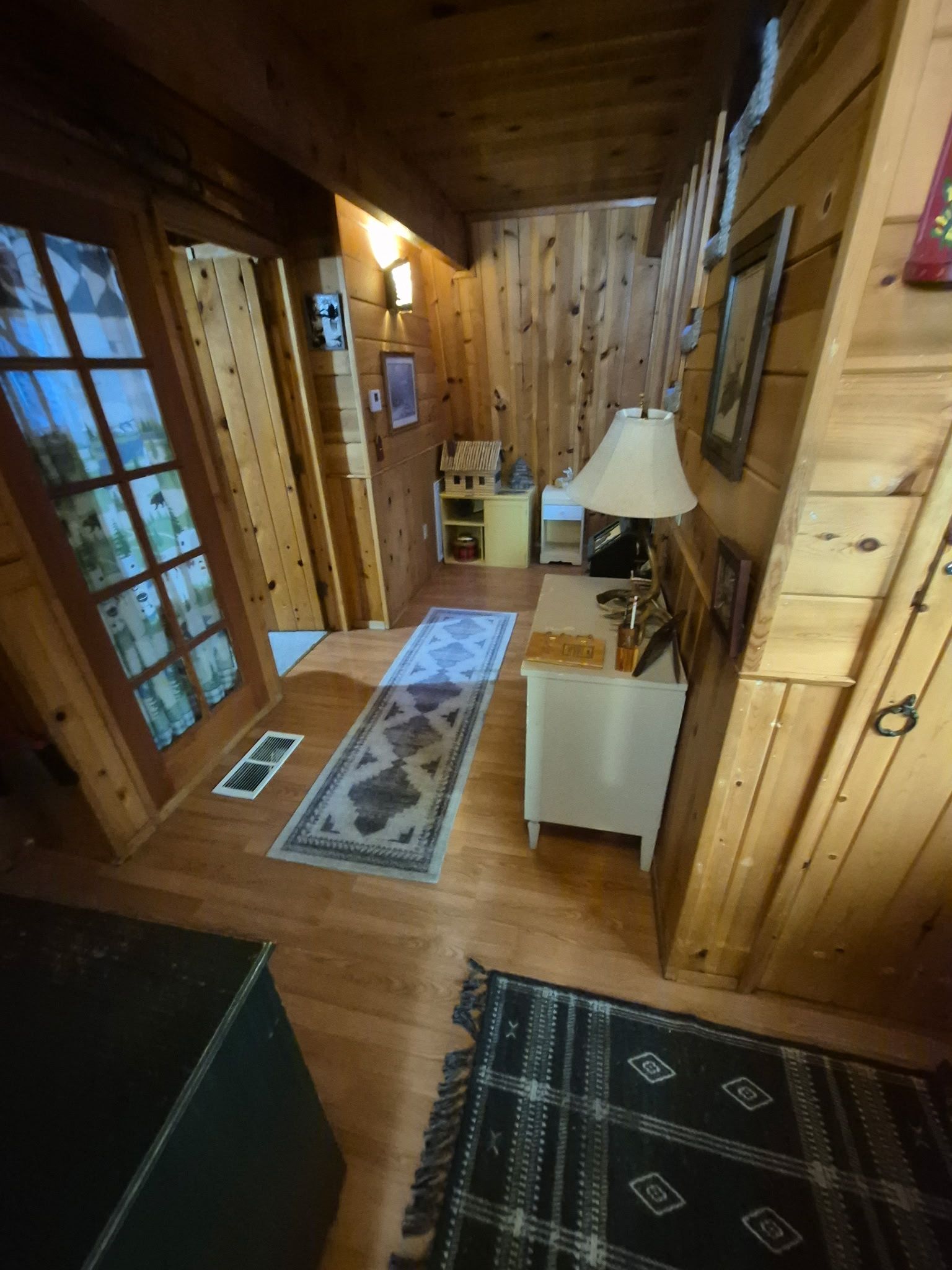 Un intérieur en bois avec un tapis au centre, une lampe et une petite table.