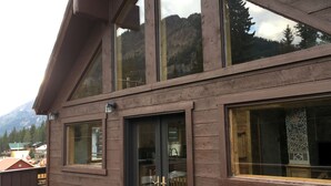 Un edificio de madera con amplios ventanales, una cocina visible y vistas a la montaña.